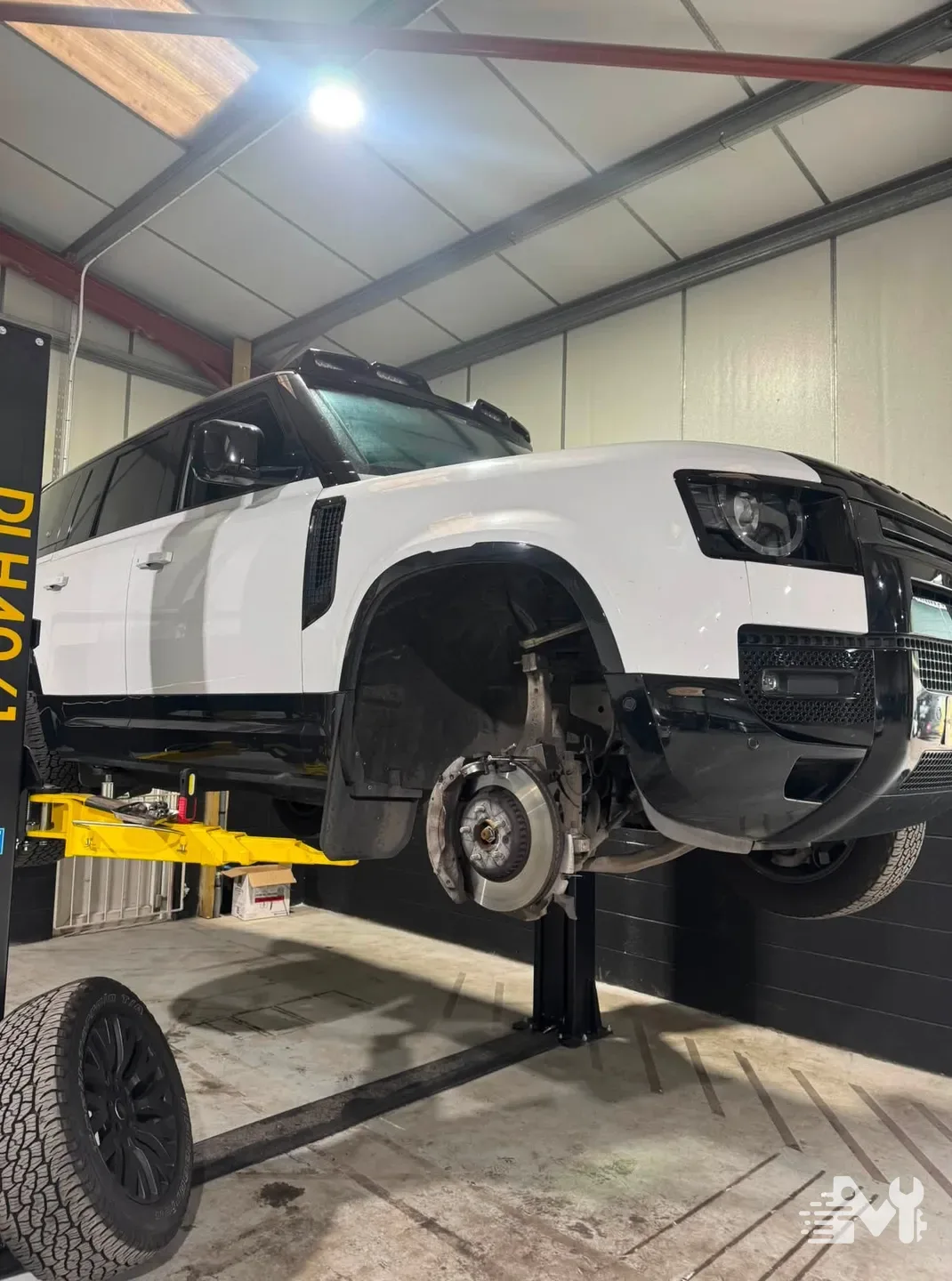 A Land Rover Defender on the two post lift at Milners, front wheel off for brake work