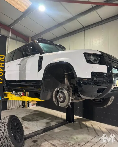 A Land Rover Defender raised on the two post lift with a wheel off, exposing the brake disc