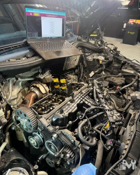 A laptop propped on the wing showing manufacturer torque data while the cam belt is set up