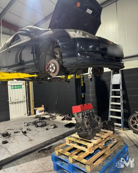 A car raised on the two post lift with its engine out and sitting on a pallet below
